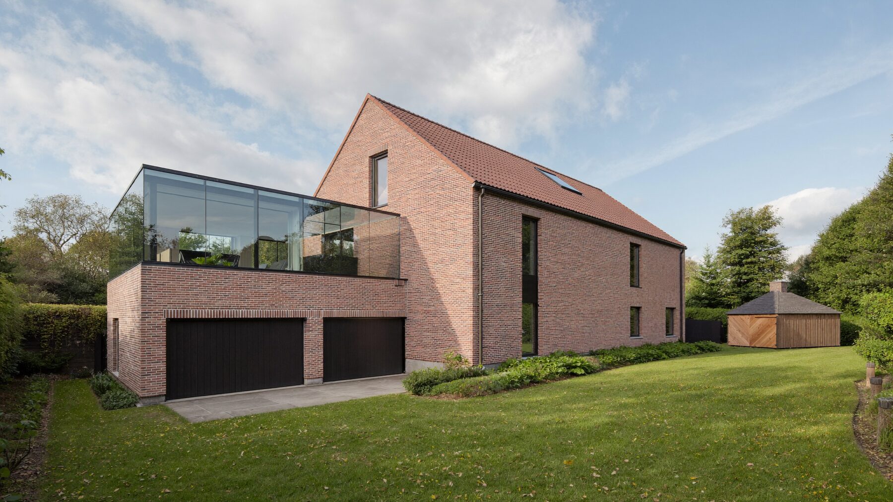 Maison en brique avec extension vitrée, double garage, abri de jardin et fenêtre de toit
